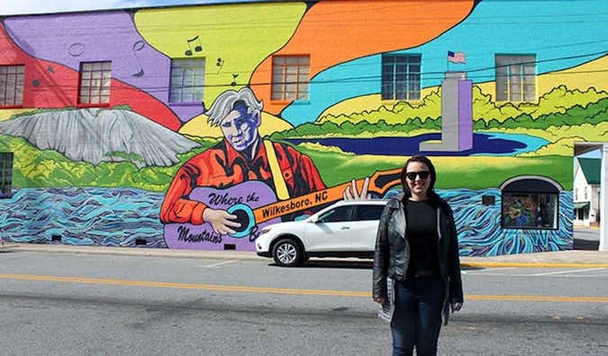 Caroline Eubanks standing in front of a mural for Doc Watson in Wilkesboro, North Carolina