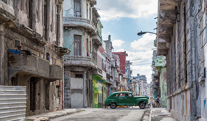 a green car driving by on a street in Havana