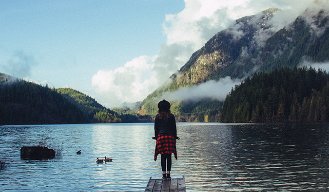 a woman standing at the end of a dock overlooking an alpine lake