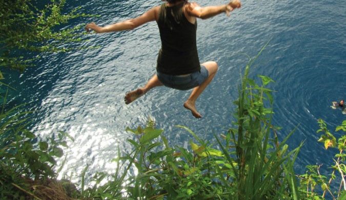 Girl traveler jumping off a cliff into Caribbean waters