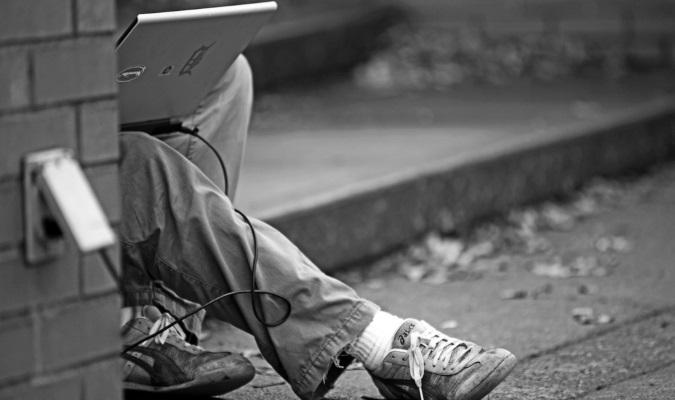 Traveler plugging laptop into a public outlet outside, bad cyber security practice