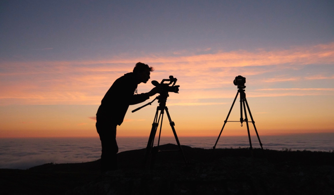A man taking photos on a mountain with two large cameras at sunrise