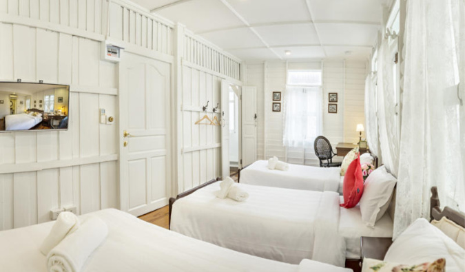 3 twin beds in an all-white room at Baan Kachitpan in Bangkok.