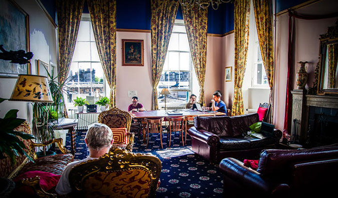 Cozy common room with leather couches, big armchairs, a communal table, and tall windows at Castle Rock in Edinburgh