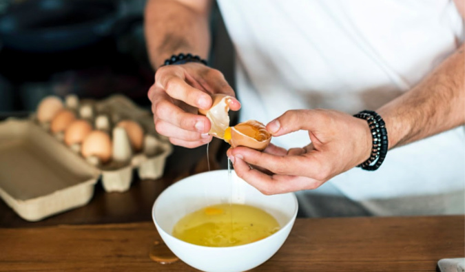 making breakfast at home by cracking eggs into a bowl