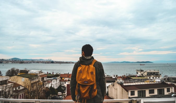 A backpacker standing at the edge of a town overlooking the water