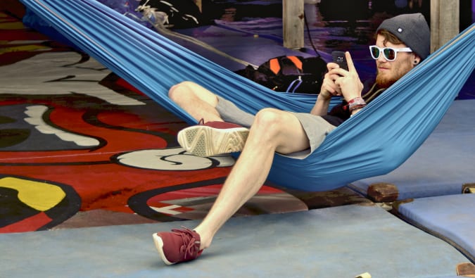 A budget traveler sitting in a hammock on their phone