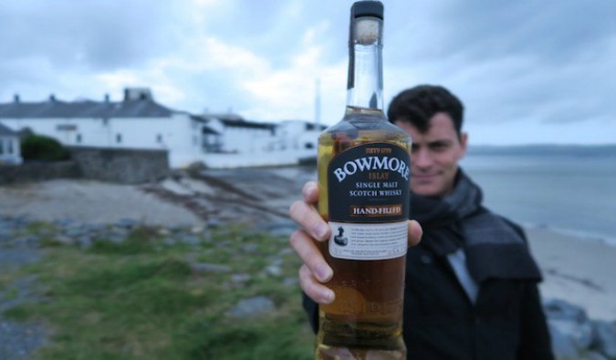 Nomadic Matt on the Isle of Islay in Scotland holding a bottle of Scotch