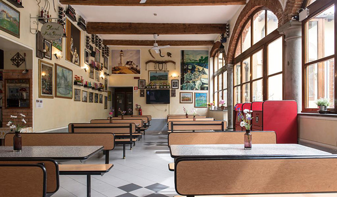 Cafeteria area with many long tables, art on the walls, and arched windows at Archi Rossi hostel in Florence, Italy