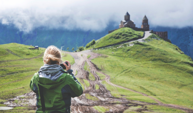 A solo traveler taking a photo of a castle on a hill