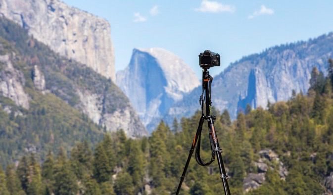 Camera and tripod set up in front of a mountain and nature