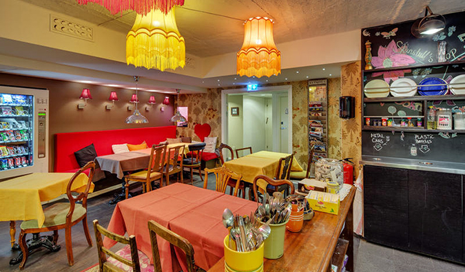 Eclectic dining area with lots of tables covered in bright table cloths and hanging lamps of different colors at Skanstull Hostel, Stockholm