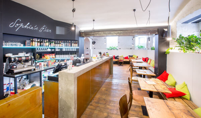 Café area with bar and lots of wooden tables, benches, and chairs at Sophie's Hostel in Prague