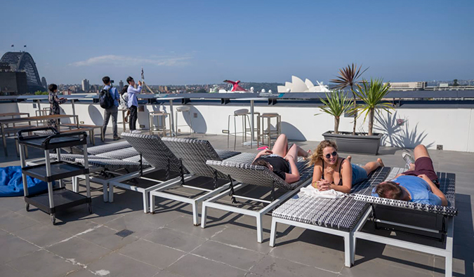 Rooftop terrace with people sunbathing on loungers at Sydney Harbor YHA hostel in Sydney, Australia