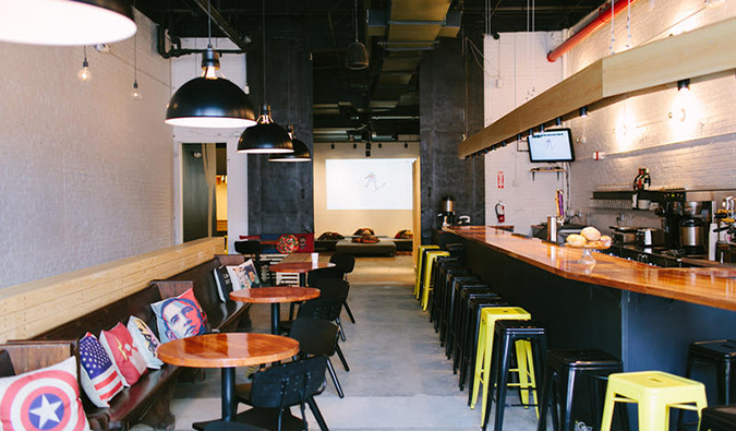 Common area with small tables and long wooden bar at The Local NYC in Queens, New York.