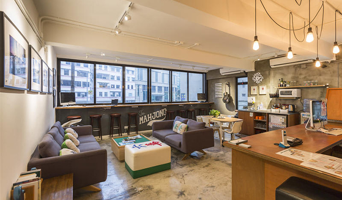 Spacious common room with couches, kitchenette area, and wall of windows at The Mahjong, Hong Kong