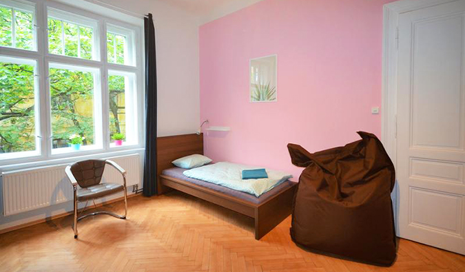 Room with pink walls, bean bag chair, twin bed, and large windows at Travel and Joy Hostel in Prague