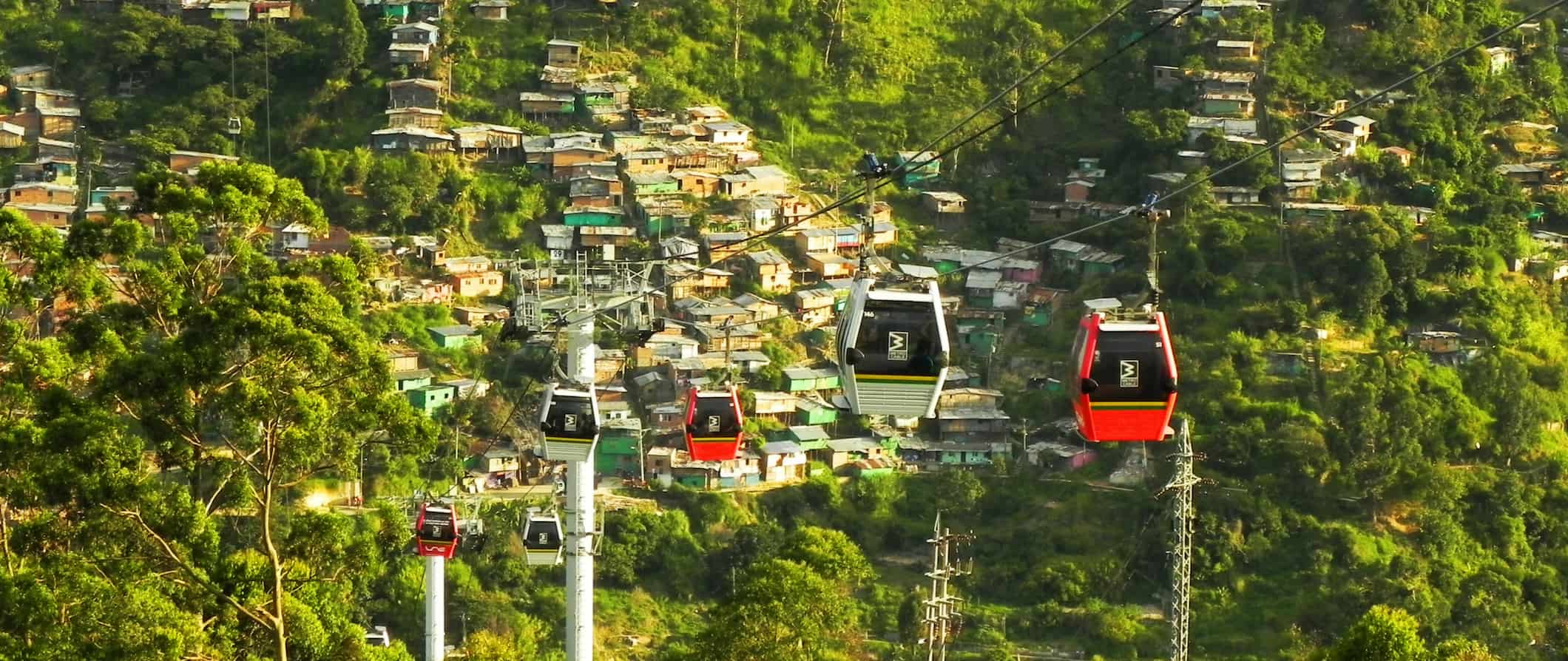 A city view of the cable cars in Medellín, Colombia surrounded by lush greenery and small houses built into the mountainside