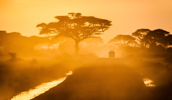 A lone jeep on a dusty road during a bright sunset in Africa