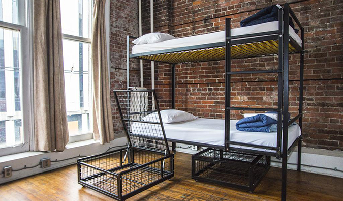Dorm room with industrial-style metal bunk beds, tall windows, and exposed brick walls at Cambie Hostel  Gastown, Vancouver