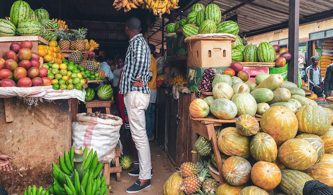 a man in Rwanda standing in a supermarket surrounded by fresh fruit