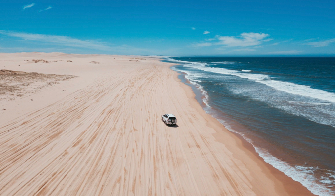 A wide open beach in Australia with a 4x4 vehicle driving in the sand