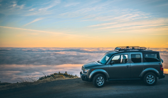 A car rental parked near a beautiful view surrounded by clouds