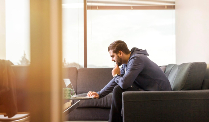 A man sitting alone on a couch working on his laptop