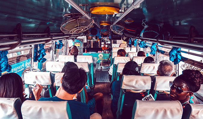 people aboard a crowded bus in Thailand with fans attached to the ceiling
