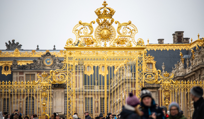 The extravagant gates of the Palace of Versailles in France surrounded by visitors