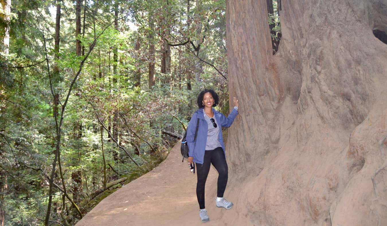 Senitra, a solo black female traveler posing by a huge tree