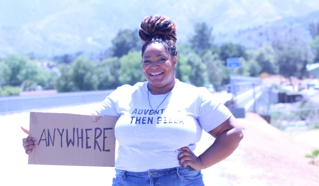 Annette posing while holding a hitchhiking sign