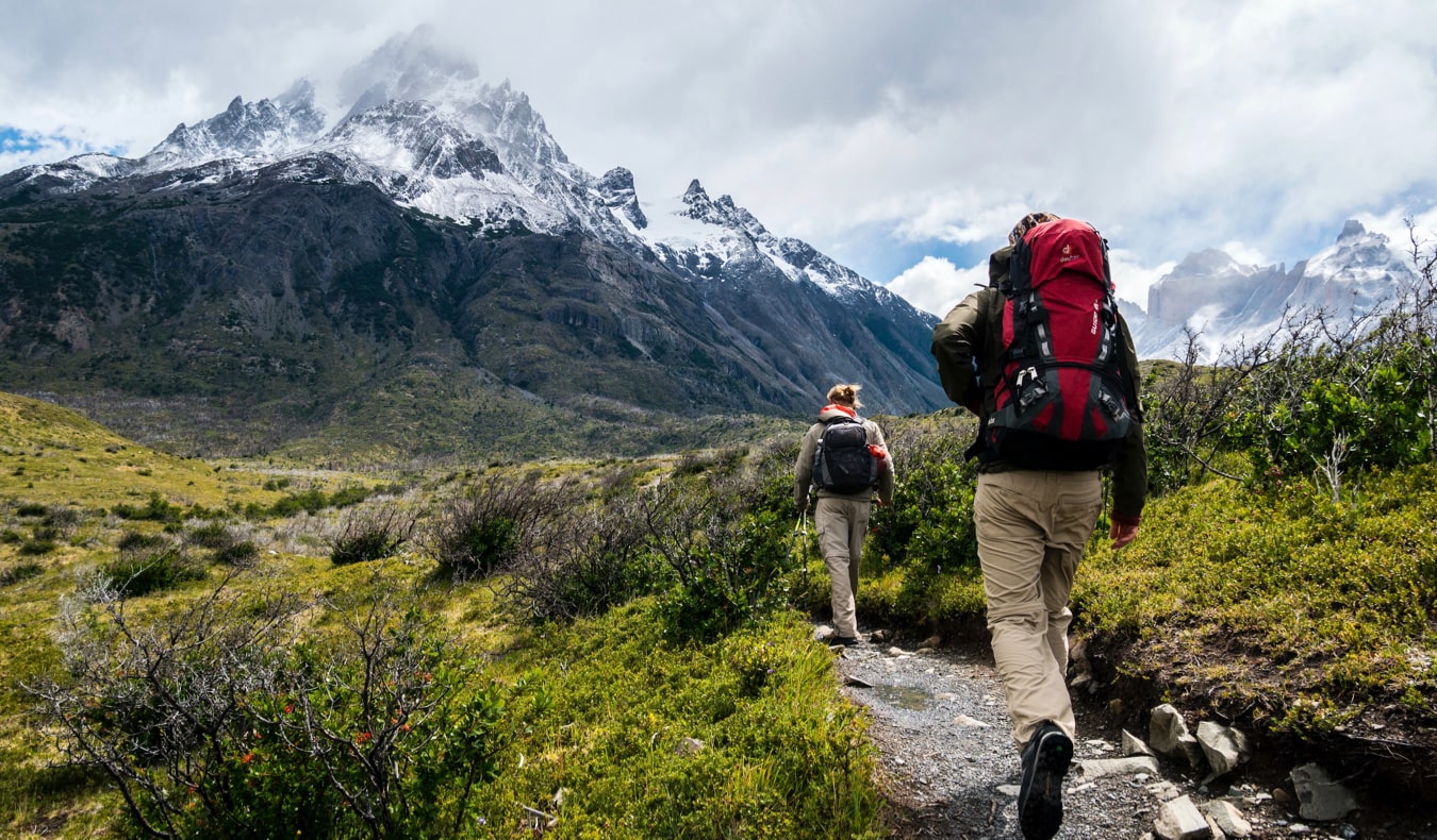 A hiker walking on a trail toward snow-capped mountains