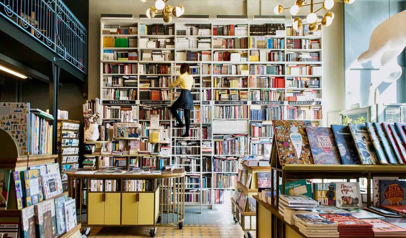 A woman in a bookstore looking at books on a ladder