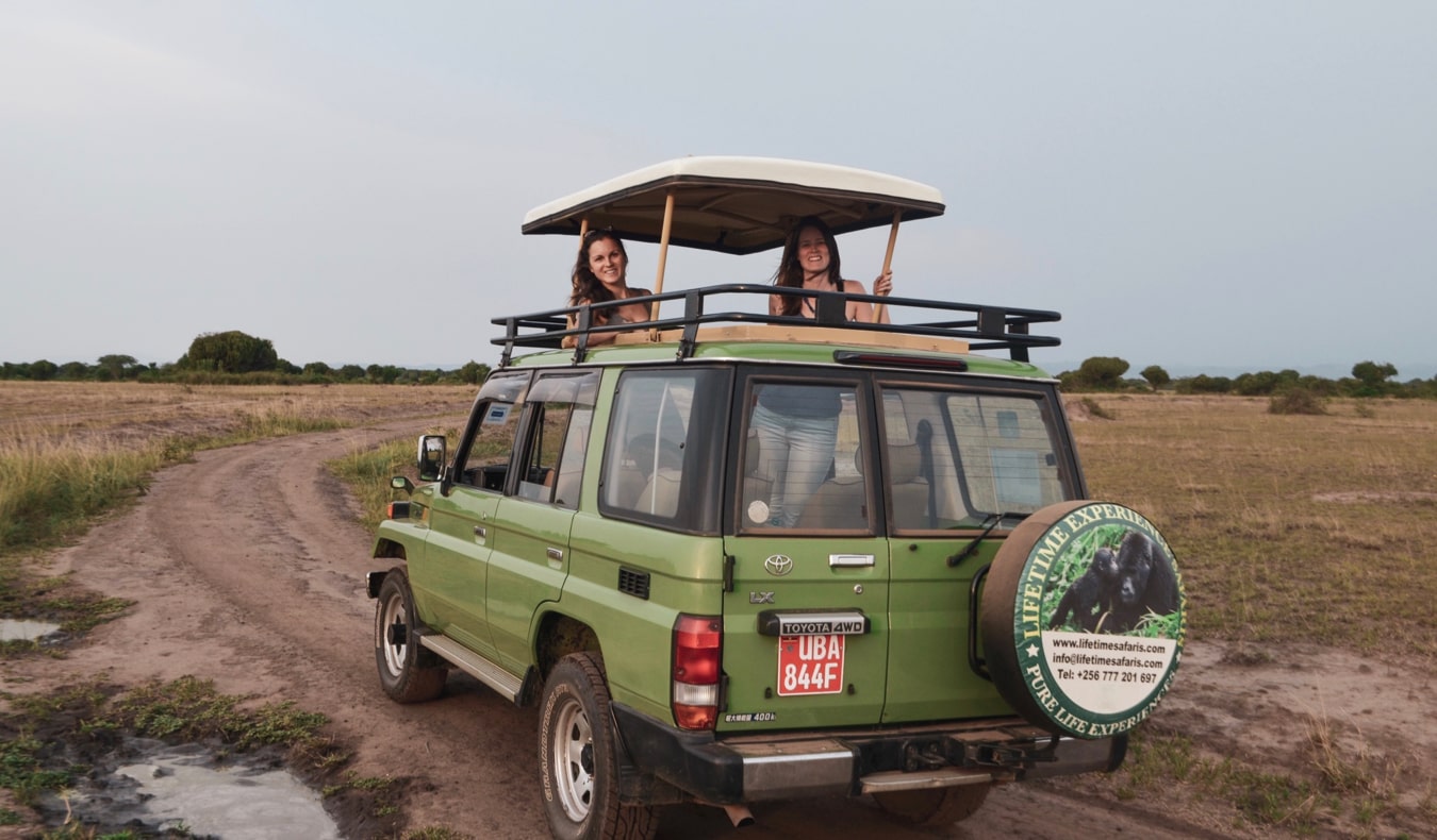 Two female travelers on safari in Uganda standing in a jeep