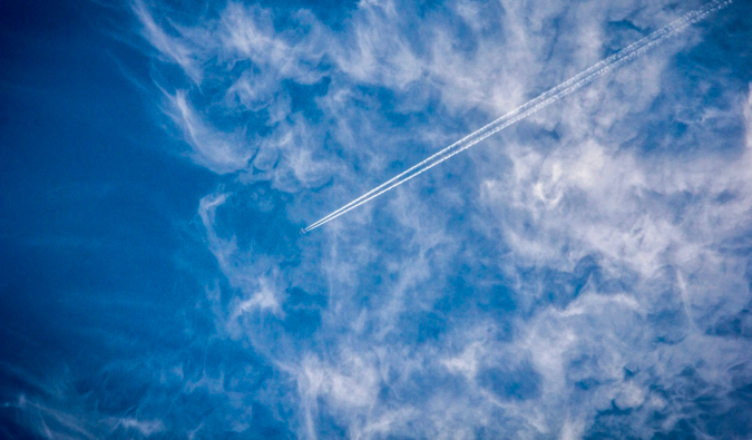 A commercial airplane high in the sky, cutting the the clouds and a blue sky