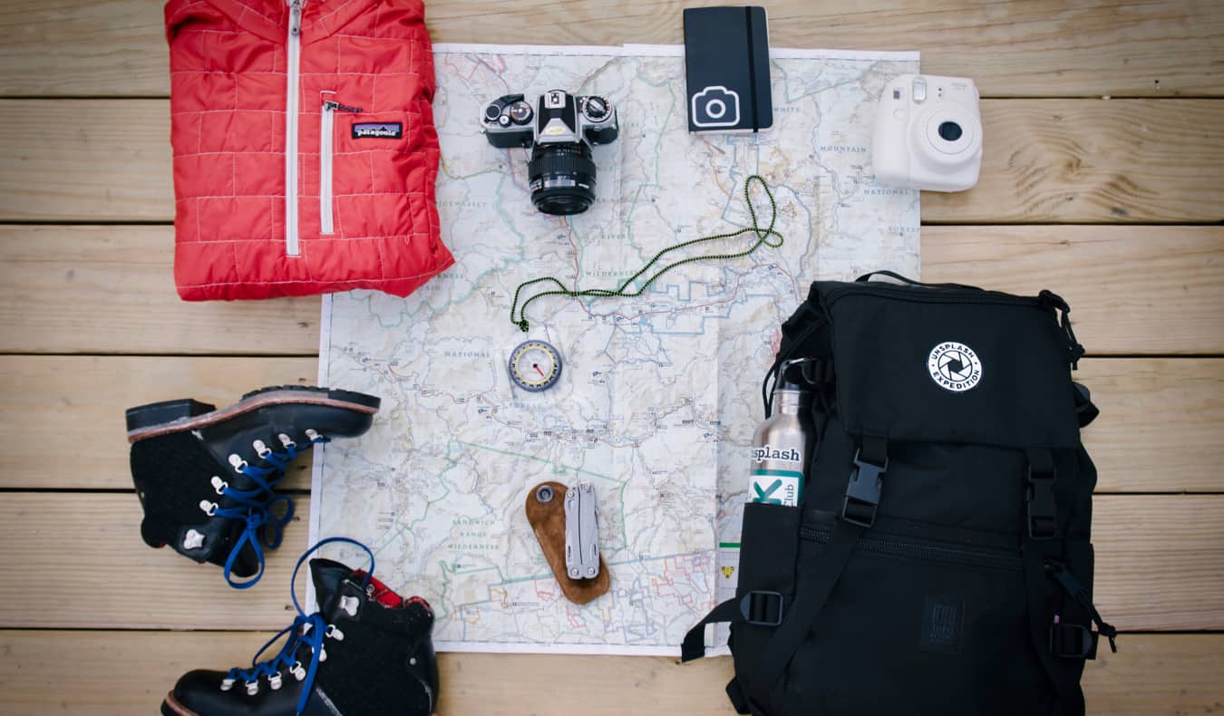 A bunch of travel gear laid out on the floor, including maps and hiking boots