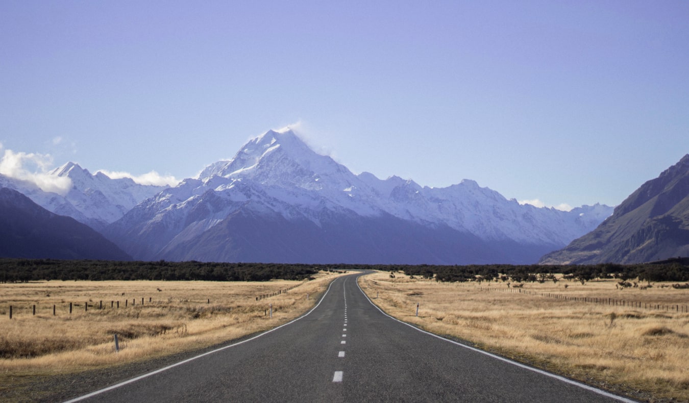 The wide open road in New Zealand with snow-capped mountains in the distance