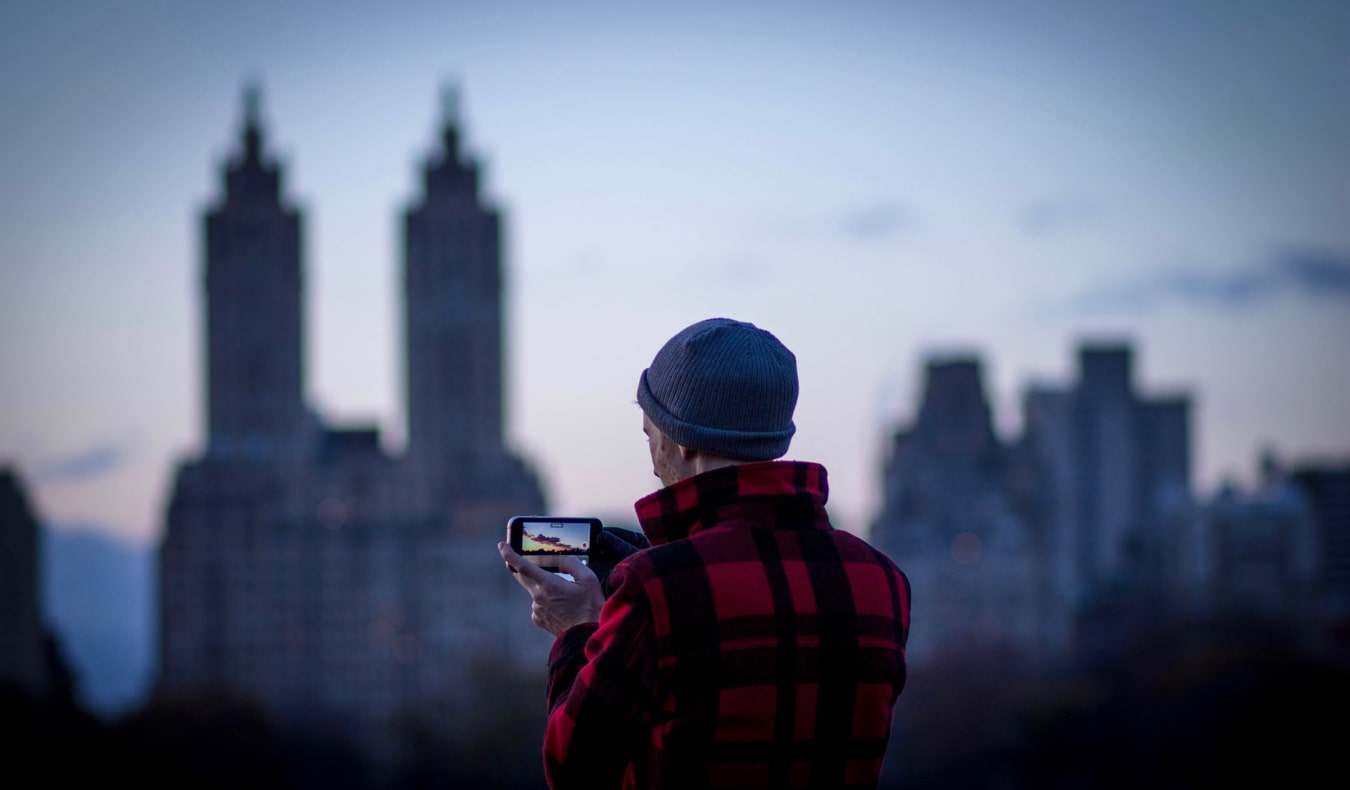 A traveler taking a photo with a smartphone at sunset