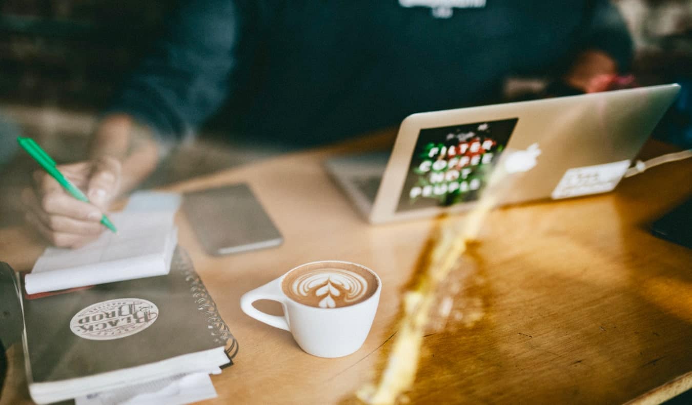 Un homme travaillant en ligne dans un café tout en buvant un café au lait.