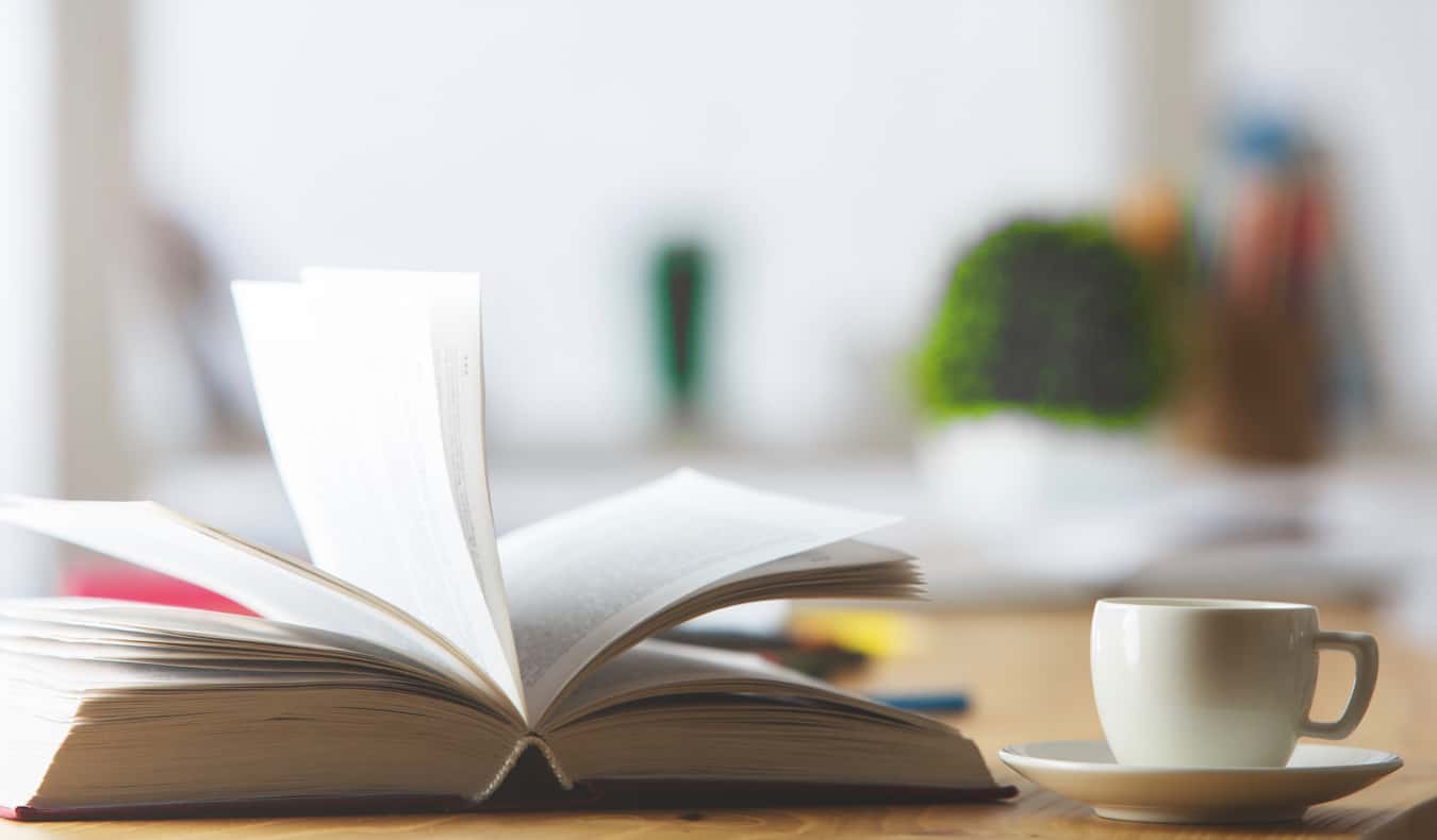 A book and a cup of tea on a desk in a well-lit office room