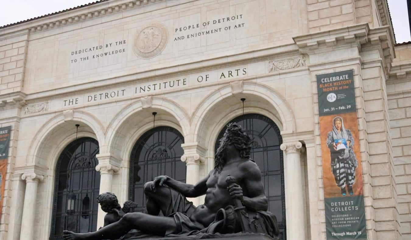 The historic exterior of the Detroit Institute of Arts with a dark statue in the foreground