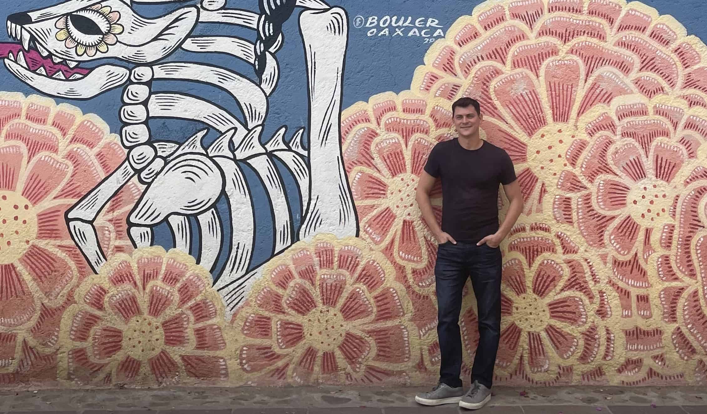 Nomadic Matt standing in front of skeletal and floral street art in Oaxaca, Mexico