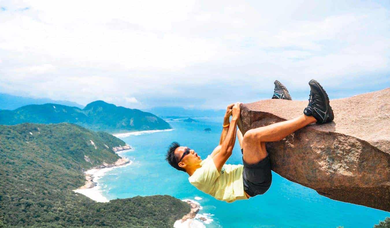 Rax, a solo digital nomad, hanging off a rock abroad