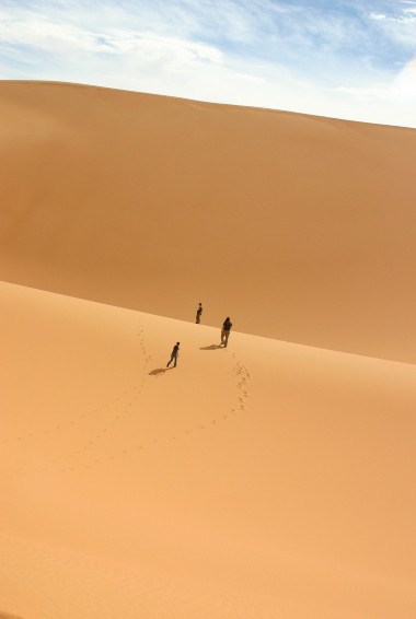 people trekking across a sand dune in the Sahara Desert