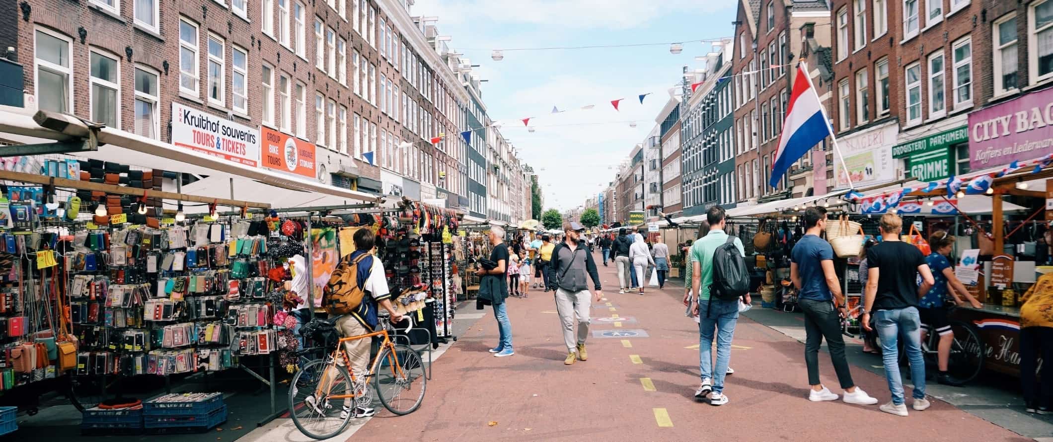 People walking down a pedestrianized street lined with market stalls in Amsterdam, the Netherlands.
