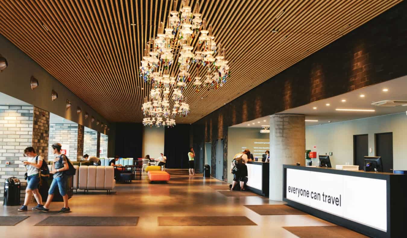 A spacious lobby with chandeliers and a reception desk that reads "Everyone Can Travel" at the a&o hostel in Venice, Italy.