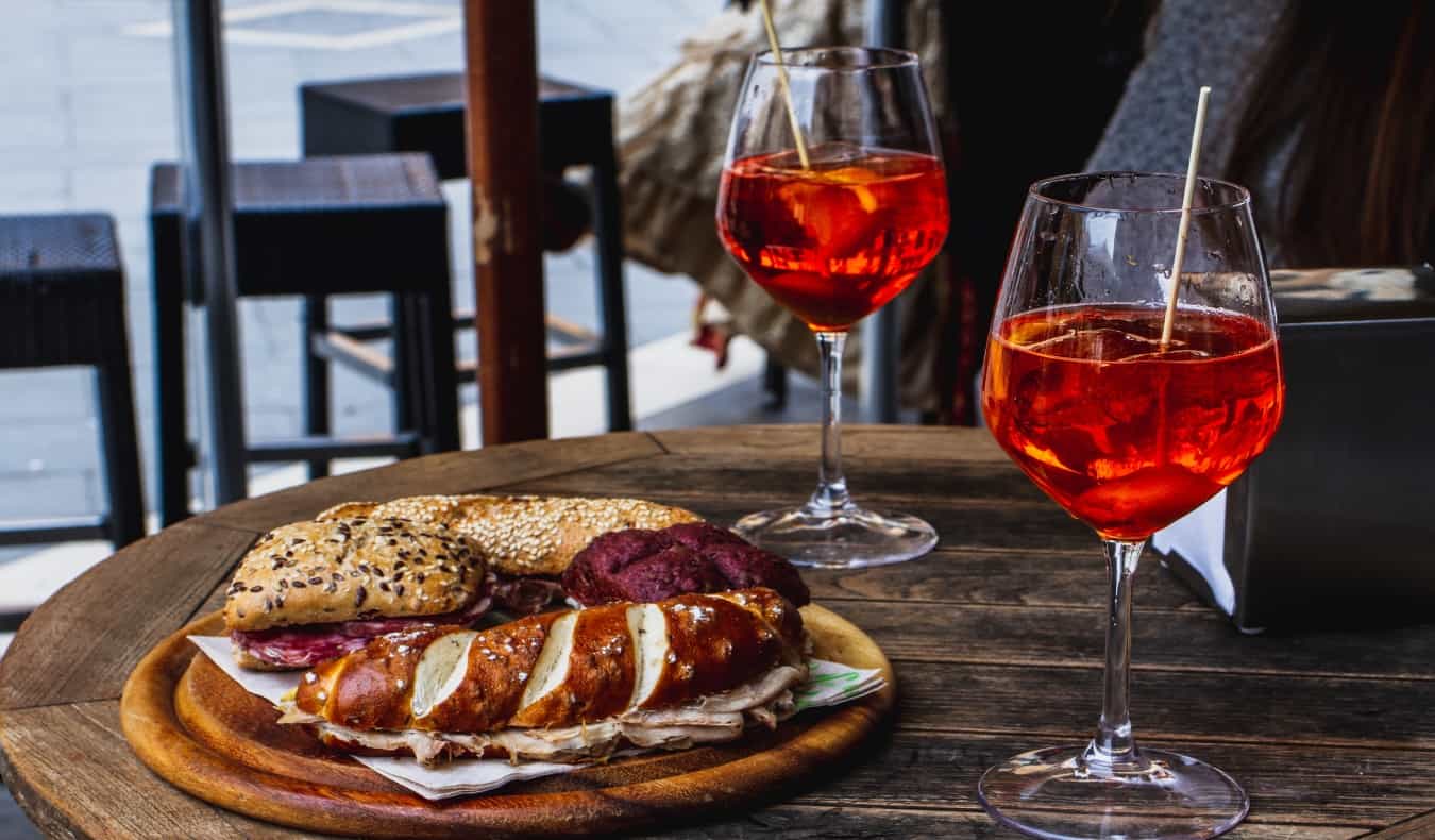 Two glasses of aperol spritz and wooden plate with sandwiches.