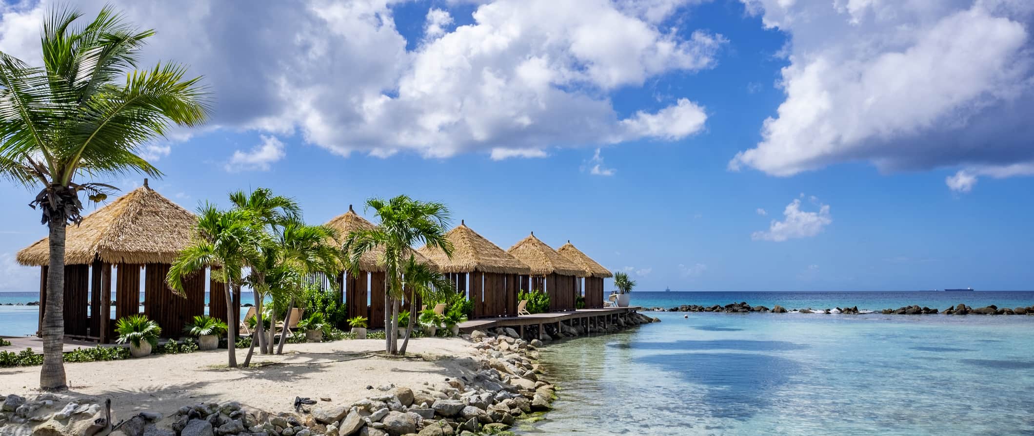 Relaxing beach bungalows and shaded lounge chairs on the sunny coast of Aruba in the Caribbean