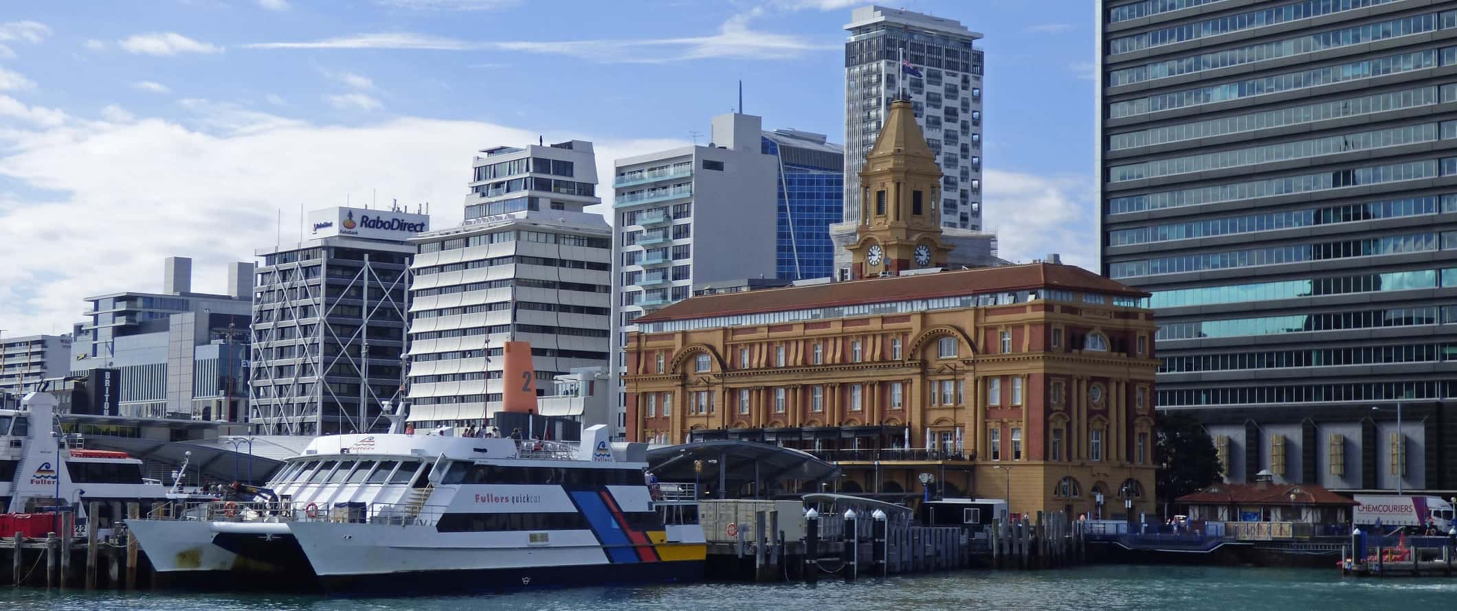 Harborfront with ferry, historic building, and tall skyscrapers in the background in Auckland, New Zealand.